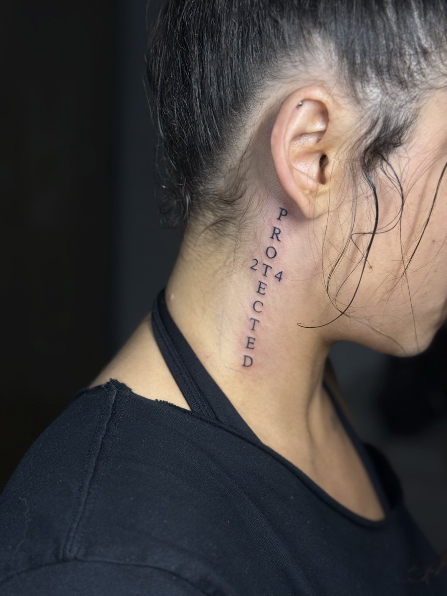 Vertical Protected lettering tattoo with 214 behind the ear.