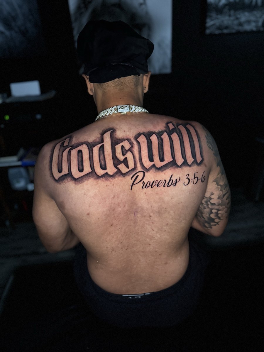 Large blackletter Godson tattoo across the upper back.