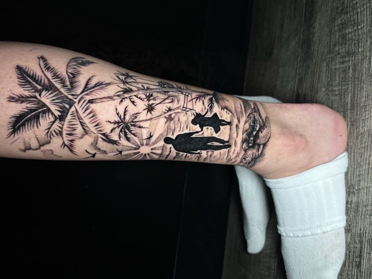Black and grey island landscape tattoo wrapping a forearm.