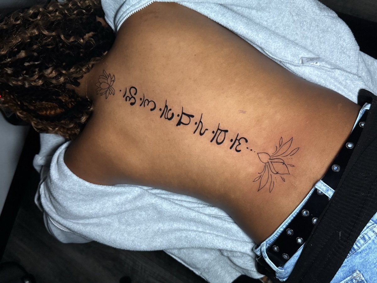 Fine script tattoo following the side of the torso.