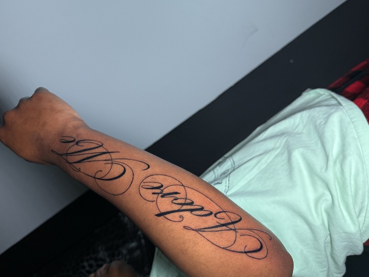 Flowing script lettering tattoo along a forearm.