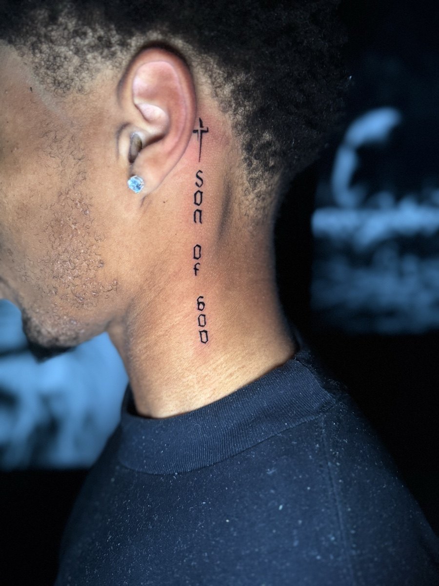 Vertical fine lettering tattoo behind the ear.
