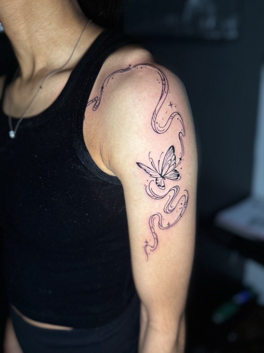 Fine-line butterfly and botanical tattoo on an upper arm.