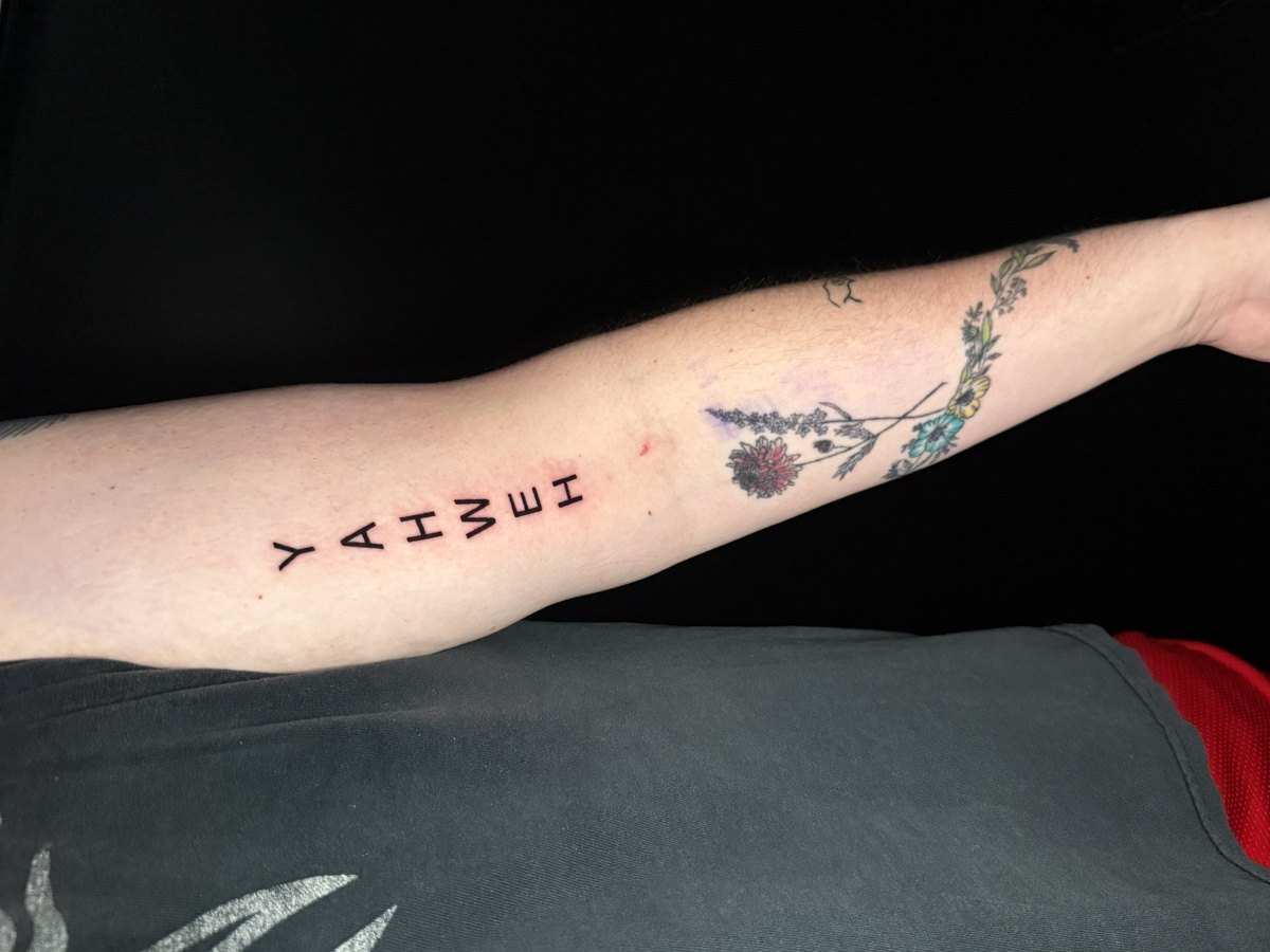 Fine-line symbols and small lettering tattoos along a forearm.